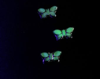 May include: Three butterfly-shaped accessories with a silver outline glow against a black backdrop. The butterflies have a bright green centre and a subtle purple glow around the edges, creating a striking contrast.