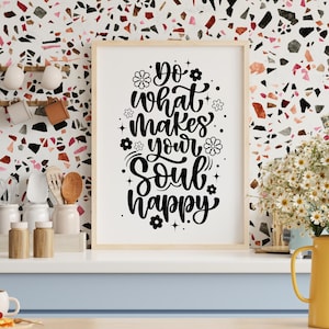 May include: A framed print with the text "Do what makes your soul happy" in black script and floral accents. The artwork is displayed on a white surface with a light wood frame, against a colorful mosaic wall.