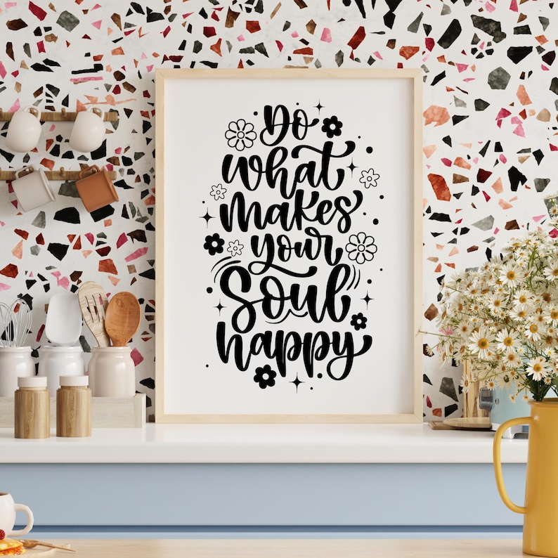 May include: A framed print with the text "Do what makes your soul happy" in black script and floral accents. The artwork is displayed on a white surface with a light wood frame, against a colorful mosaic wall.