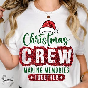 May include: White t-shirt featuring a Christmas design. The graphic includes a Santa hat, the words "Christmas CREW" in green and red glitter, and the phrase "MAKING MEMORIES TOGETHER".