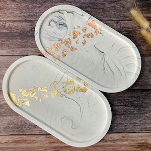 Op de afbeelding: Twee ovale witte hars trays met gouden blad accenten. De trays hebben een marmerpatroon en zijn perfect voor het serveren van snacks of het presenteren van kleine items.