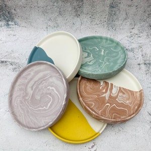 Puede incluir: Cinco posavasos redondos de hormigón decorativos con patrones de mármol. Los posavasos son de varios colores, incluyendo azul claro, verde, morado, marrón y amarillo.