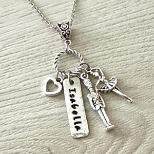 May include: Silver necklace with a charm that says "Isabella" and other charms including a heart, a nutcracker, and a ballerina.