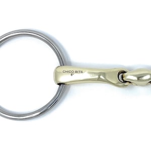 May include: A gold-colored horse bit with a stainless steel mouthpiece. The bit has a loose ring on each end and the text "CHICO BITS F" is engraved on one side.