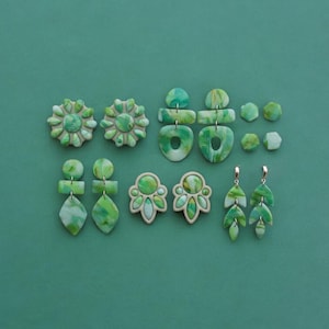 Könnte beinhalten: Eine Sammlung handgefertigter Polymer-Ton-Ohrringe in verschiedenen Formen und Designs. Die Ohrringe weisen Grüntöne mit Marmormustern auf. Stile umfassen Blumen-, geometrische und Blattformen. Der Hintergrund ist ein einfarbiger Türkiston.