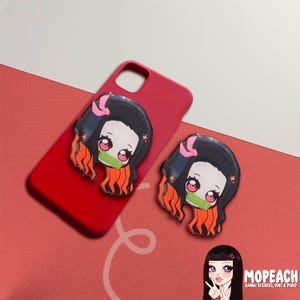 May include: Red phone case with two anime character stickers. The stickers are of a girl with pink hair and a girl with red hair. The stickers are both wearing green masks.