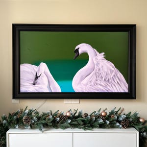 May include: A framed painting of two white swans with black eyes, one swan is facing the viewer and the other is facing away. The swans are on a green and blue background.