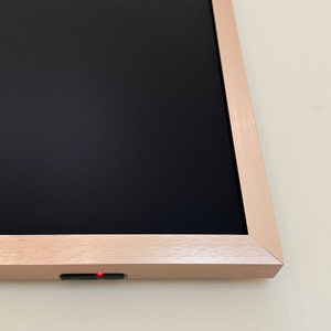Puede incluir: Un marco de fotos digital con marco de oro rosa, pantalla negra y una luz roja en el borde inferior.