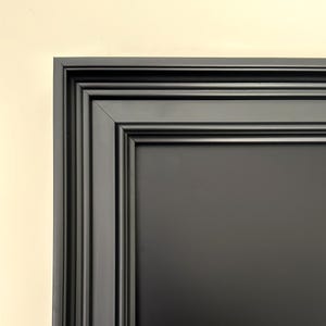 Puede incluir: Un marco de fotos negro con un grueso moldura ornamentado. El marco tiene un diseño simple y limpio y es perfecto para mostrar fotos, obras de arte u otros artículos decorativos.