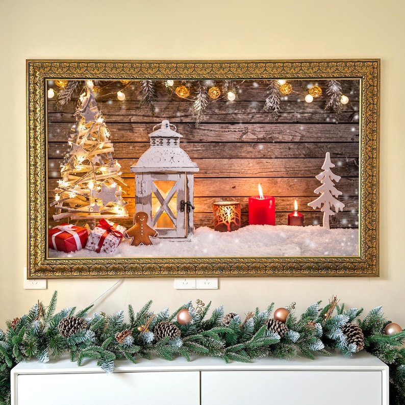 May include: A framed Christmas scene with a rustic wooden background. It features a white lantern, lit candles, a gingerbread man, and a small Christmas tree. Presents and decorative lights add to the festive atmosphere. The frame is gold.