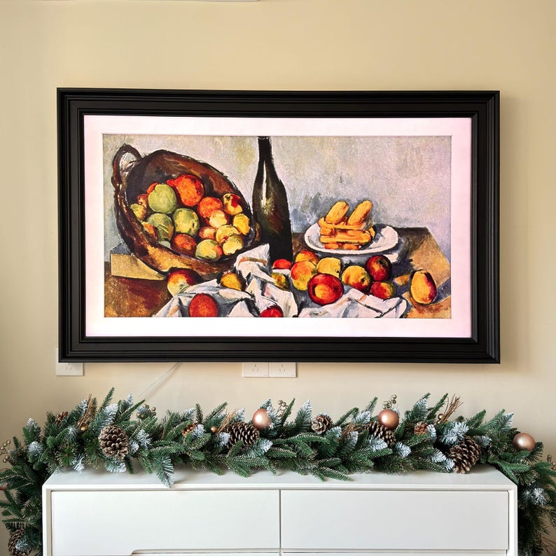 May include: A framed painting of a still life with a basket of apples, a bottle of wine, and a plate of pastries. The painting is in a dark wood frame and is hanging on a wall.