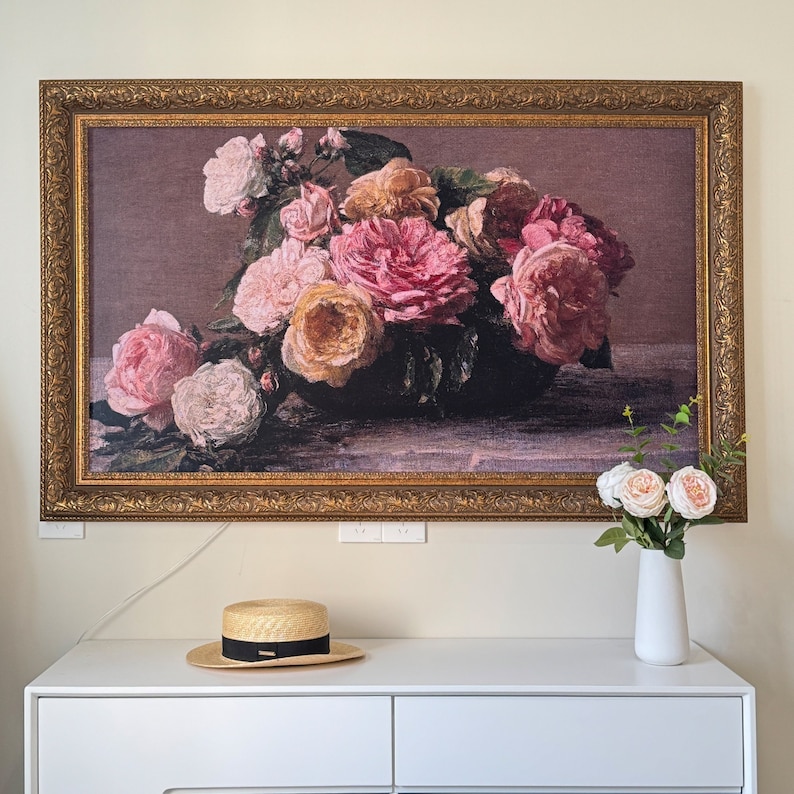 May include: A framed print of a still life featuring a bouquet of pink and white roses in a vintage gold frame. The roses are arranged in a vase and are surrounded by green leaves.