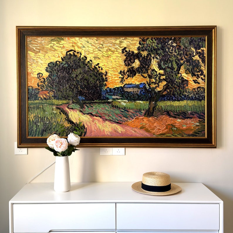 May include: A framed oil painting depicting a landscape with two trees and a house in the distance. The painting is set against a yellow sky with a hint of orange and blue. The trees are green and brown, and the house is white with a brown roof. The painting is framed in a dark brown wood frame.