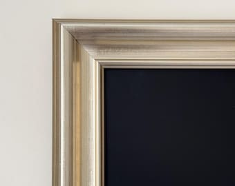May include: A black framed chalkboard with a silver-colored frame. The frame has a decorative, raised edge.
