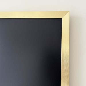 Puede incluir: Una pizarra negra enmarcada con un marco de metal dorado.