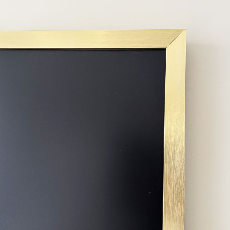 Puede incluir: Una pizarra negra enmarcada con un marco de metal dorado.