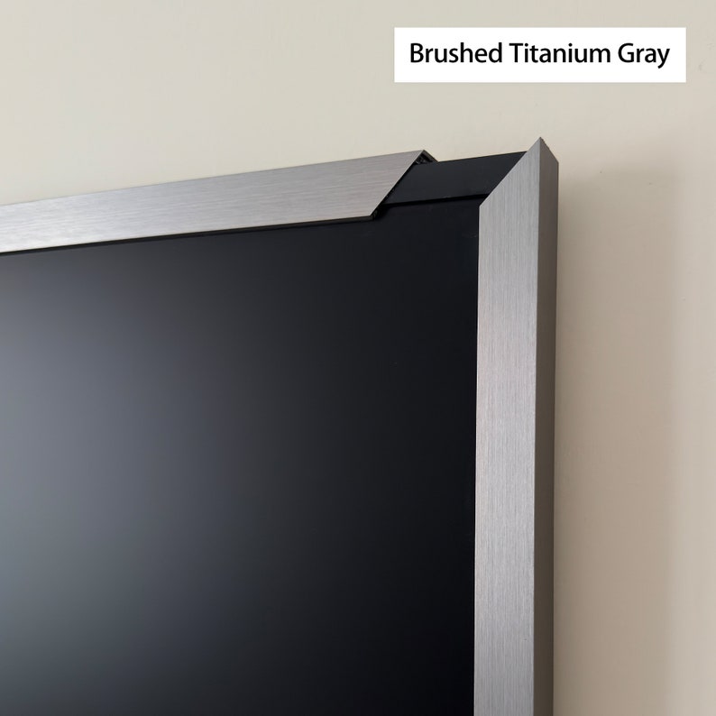 Puede incluir: Primer plano del borde superior de un televisor con marco negro y un marco de metal gris titanio cepillado. El marco tiene una textura sutil.