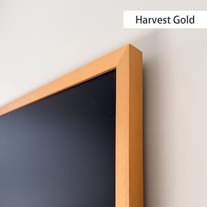 Può includere: Una cornice rettangolare in legno marrone chiaro con interno blu navy scuro. La cornice è appoggiata a una parete bianca. Il testo "Harvest Gold" è visualizzato in un rettangolo bianco nell'angolo in alto a destra.