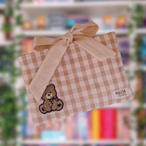 Könnte beinhalten: Eine hellbraune und weiße Vichy-Karo-Buchhülle mit einer beigen Schleife. Auf der Vorderseite befindet sich ein Teddybär-Aufnäher. Der Text "NALISA Creates" befindet sich in der unteren rechten Ecke.
