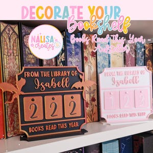 Könnte beinhalten: Ein schwarzer und kupferfarbener Bücherregal-Zähler mit dem Text "From the Library of Isabell" und "Books Read This Year". Der Zähler zeigt die Zahl 222 an. Ein rosa Bücherregal-Zähler zeigt die Zahl 123 an.