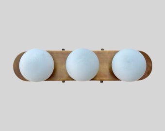 May include: A brass light fixture with three frosted glass globes. The fixture is oval shaped and has a brushed brass finish.