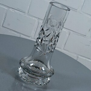 Könnte beinhalten: Eine klare Glasvase mit einem geschliffenen Glasdesign mit einem floralen Muster. Die Vase hat einen breiten Boden und einen schmalen Hals.