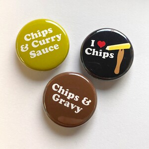 May include: Three round button pins with different designs. The first pin is yellow-green with white text that reads "Chips & Curry Sauce". The second pin is black with white text that reads "I ♥ Chips" and a yellow stick of butter with a red heart on top of a wooden fork. The third pin is brown with white text that reads "Chips & Gravy".