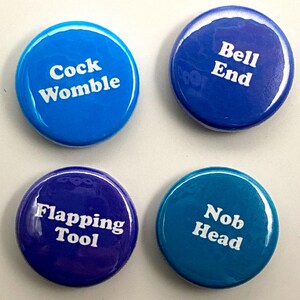 Może przedstawiać: Cztery okrągłe guziki w kolorze niebieskim, turkusowym i fioletowym z białym tekstem. Guziki mają napis "Cock Womble", "Bell End", "Flapping Tool" i "Nob Head".