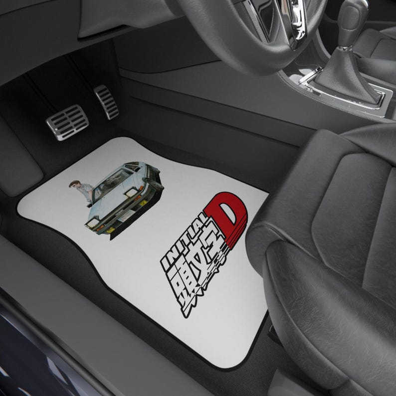 May include: White car floor mats with a black border. One mat features a light blue car graphic with a person, and the other mat has the text "INITIAL D" in red and white.