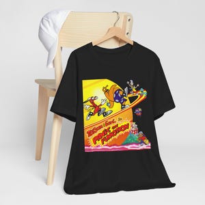May include: Black t-shirt with a cartoon graphic and the text "Tom & Jerry in Panic's on Funkotron." The graphic depicts cartoon characters on a colourful background. A white baseball cap hangs on a wooden chair.