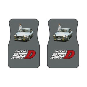 May include: Two gray car floor mats featuring a white car with a person standing next to it. The mats have the text "INITIAL D" in white and red.