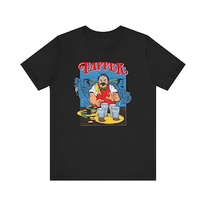 Puede incluir: Una camiseta negra con un estampado gráfico de un camarero con bigote, chaleco rojo y pajarita verde. El texto TAPPER aparece en rojo sobre el personaje, que extiende las manos hacia varios vasos sobre una barra de madera con monedas.