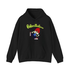 May include: Black hoodie featuring a graphic of Parappa the Rapper, a cartoon character wearing a red beanie, blue pants, and red shoes. The words "PaRappa the Rapper" are in green and yellow above the character. The hoodie has a front pocket and a drawstring hood.