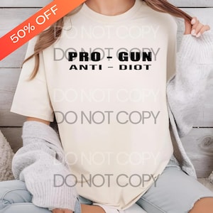 Peut inclure: T-shirt crème avec l'inscription noire "PRO - GUN ANTI - DIOT". Une bannière rouge et orange en haut à gauche indique "50% OFF". Le t-shirt est de style décontracté.