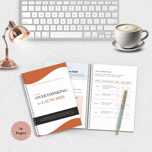 May include: An open spiral-bound workbook titled "From Overthinking to Launched" with an orange and white cover, next to a cup of coffee, a pen, and a keyboard. The workbook is designed for creators. The image also shows a rose gold desk lamp.