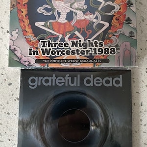 Puede incluir: Dos estuches de CD de Grateful Dead. El estuche superior presenta el texto "Grateful Dead" y "Three Nights In Worcester 1988". El estuche inferior tiene "grateful dead" y "the centrum worcester, MA, april 4th, 1987". El estuche superior tiene una ilustración colorida.