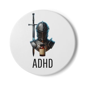 May include: A round white coaster featuring a dark metal knight helmet, a vertical sword, and a small brown glass medicine bottle. Below these items, the text ADHD is printed in a bold, black, sans-serif font. The design is centered on the coaster.