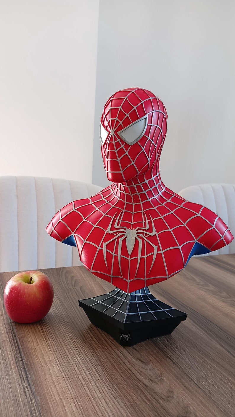 May include: A red and blue Spider-Man bust with a silver spider web design. The bust is on a black base with a spider web design.