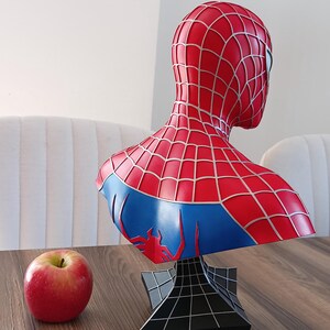 May include: A red and blue Spider-Man bust with a black web-shaped base. The bust is a collectible figure of the superhero.
