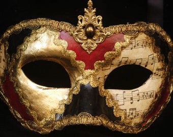 May include: A black, gold and red masquerade mask with a gold filigree design and musical notes on the right side.