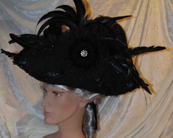 May include: A black tricorn hat with a large black feather plume and a black velvet flower with a rhinestone center.