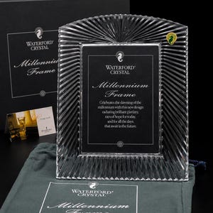 Puede incluir: Un marco de fotos de cristal transparente con un patrón de rayos de sol alrededor del borde. El centro contiene una inserción negra con el texto Waterford Crystal Millennium Frame, celebrando el amanecer del milenio con rayos de esperanza.