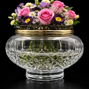 Op de afbeelding: Een heldere, geslepen glazen vaas met een gouden rand, gevuld met een levendig arrangement van roze rozen, paarse en gele bloemen. De vaas heeft een brede, afgeronde vorm.