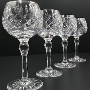 Puede incluir: Cuatro copas de vino de cristal transparente con patrones tallados en forma de diamante. Las copas tienen un cuenco redondeado, un tallo delgado y una base circular. Las copas están dispuestas en fila, enfocándose en la primera.