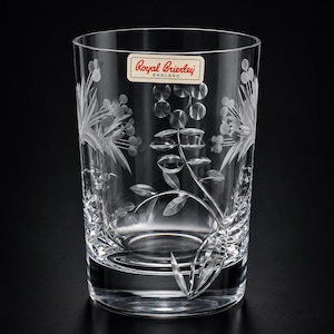 May include: A clear crystal tumbler featuring an etched floral pattern of leaves and berries. A rectangular sticker near the rim displays the text Royal Brierley ENGLAND in red and black. The glass has a thick, solid base and smooth sides.
