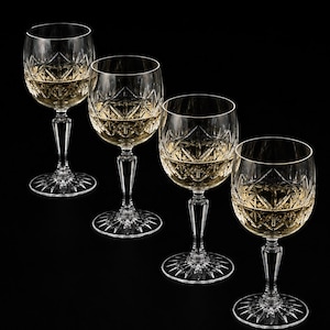 Può includere: Un set di quattro calici da vino in cristallo trasparente, ognuno caratterizzato da un dettagliato motivo a diamante e stella intagliato sulla coppa. I calici presentano uno stelo sottile e una base circolare con un design a raggiera, riempiti di liquido chiaro.