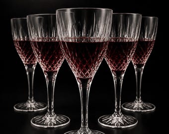 May include: A set of five clear crystal wine glasses arranged in a V-formation, each filled with deep red wine. The glasses feature a diamond-cut pattern on the lower bowl, vertical fluting near the rim, and a starburst design on the circular base.