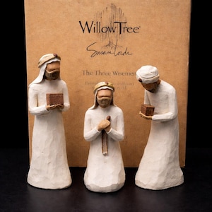Könnte beinhalten: Ein Set aus drei Willow Tree-Figuren, die die Heiligen Drei Könige darstellen, jeweils in weißen Gewändern und Kopfbedeckungen, die Geschenke halten. Die Figuren stehen vor einer braunen Schachtel mit dem Willow Tree-Logo und der Unterschrift von Susan Lordi.