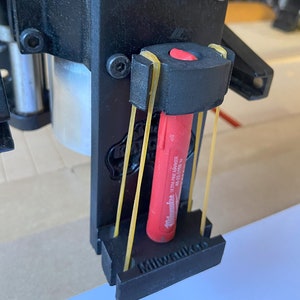 Könnte beinhalten: Ein schwarzer Kunststoff-Werkzeughalter mit einem roten und schwarzen Milwaukee Ultra Fine Marker, der mit gelben Gummibändern befestigt ist. Der Halter trägt die Aufschrift "Milwaukee" auf der Unterseite.