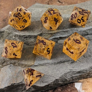 May include: Set of six gold and brown dice with black and red numbers. The dice are made of resin and have a speckled appearance.